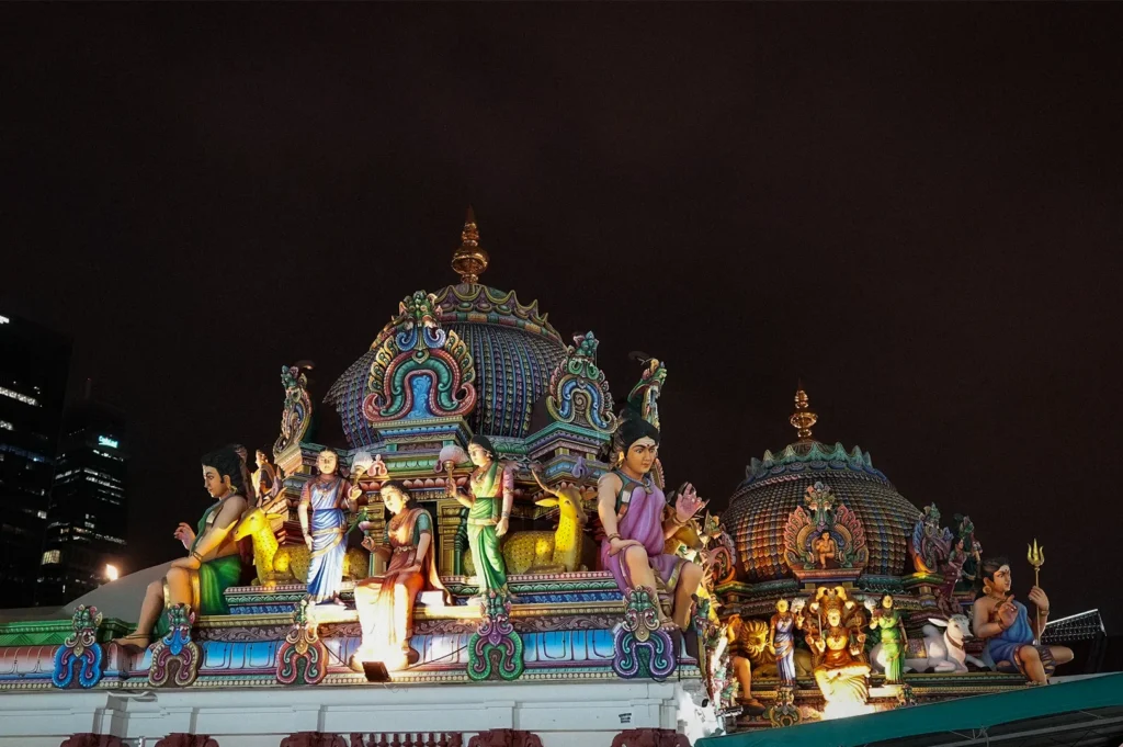 Sri Mariamman Temple in Singapore illuminated at night, featuring colorful Hindu deity sculptures, ornate temple architecture, and intricate rooftop carvings in the heart of Chinatown.