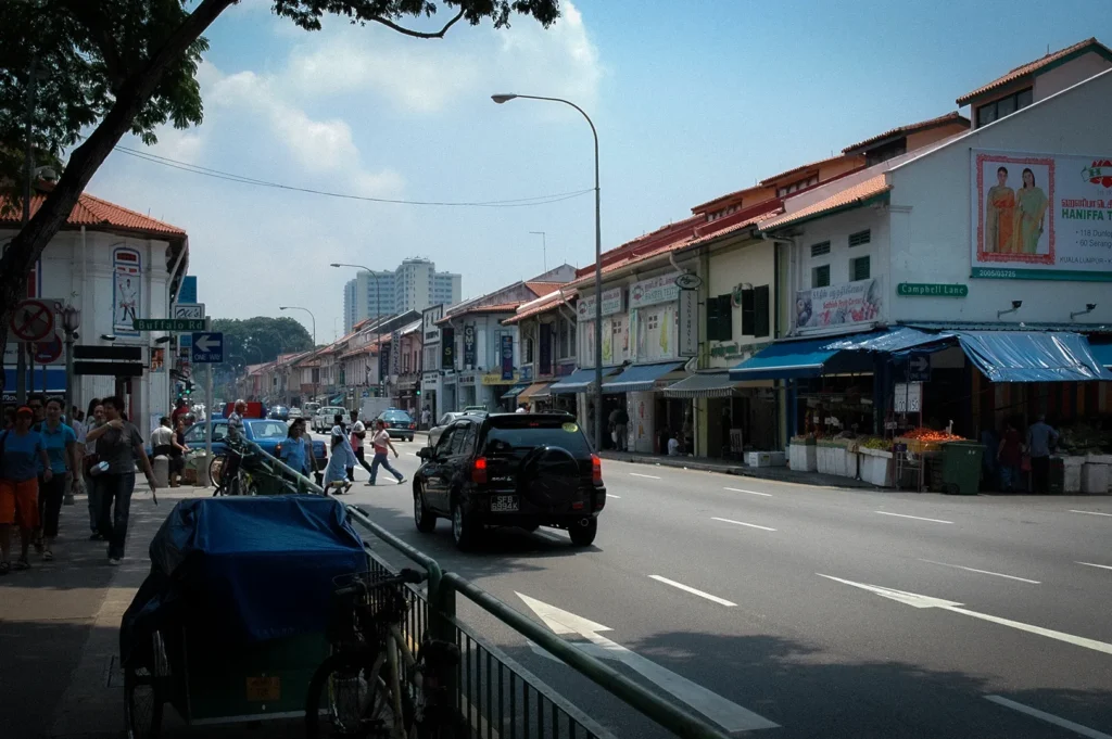 Bustling street scene in Little India, Singapore, featuring colorful heritage shophouses, local businesses, pedestrians, and traffic along a vibrant cultural district known for shopping and dining.