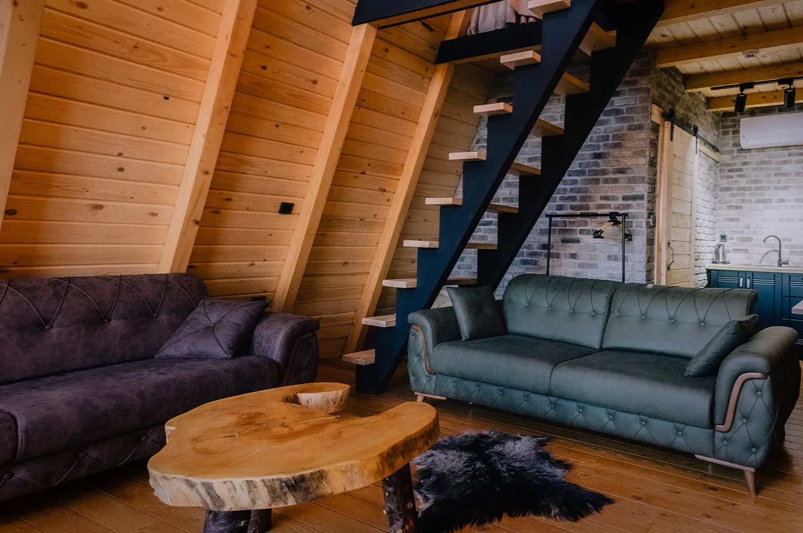 Modern wooden chalet interior featuring cozy sofas, loft staircase, exposed timber walls, and an open-plan living space with rustic contemporary design.