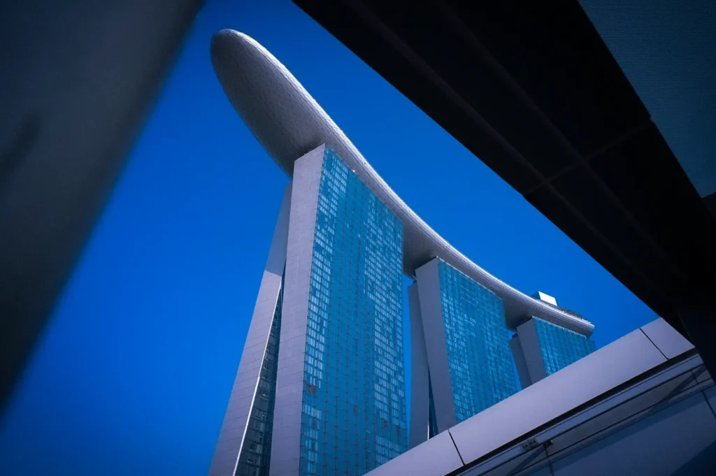 Low-angle view of Marina Bay Sands in Singapore framed by modern architecture, highlighting the iconic SkyPark against a clear blue sky.