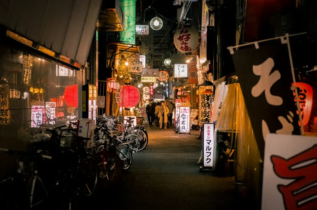 Traditional Japanese izakaya alley at night with glowing lanterns, restaurant signs, bicycles, and lively dining spots creating an authentic nightlife atmosphere.