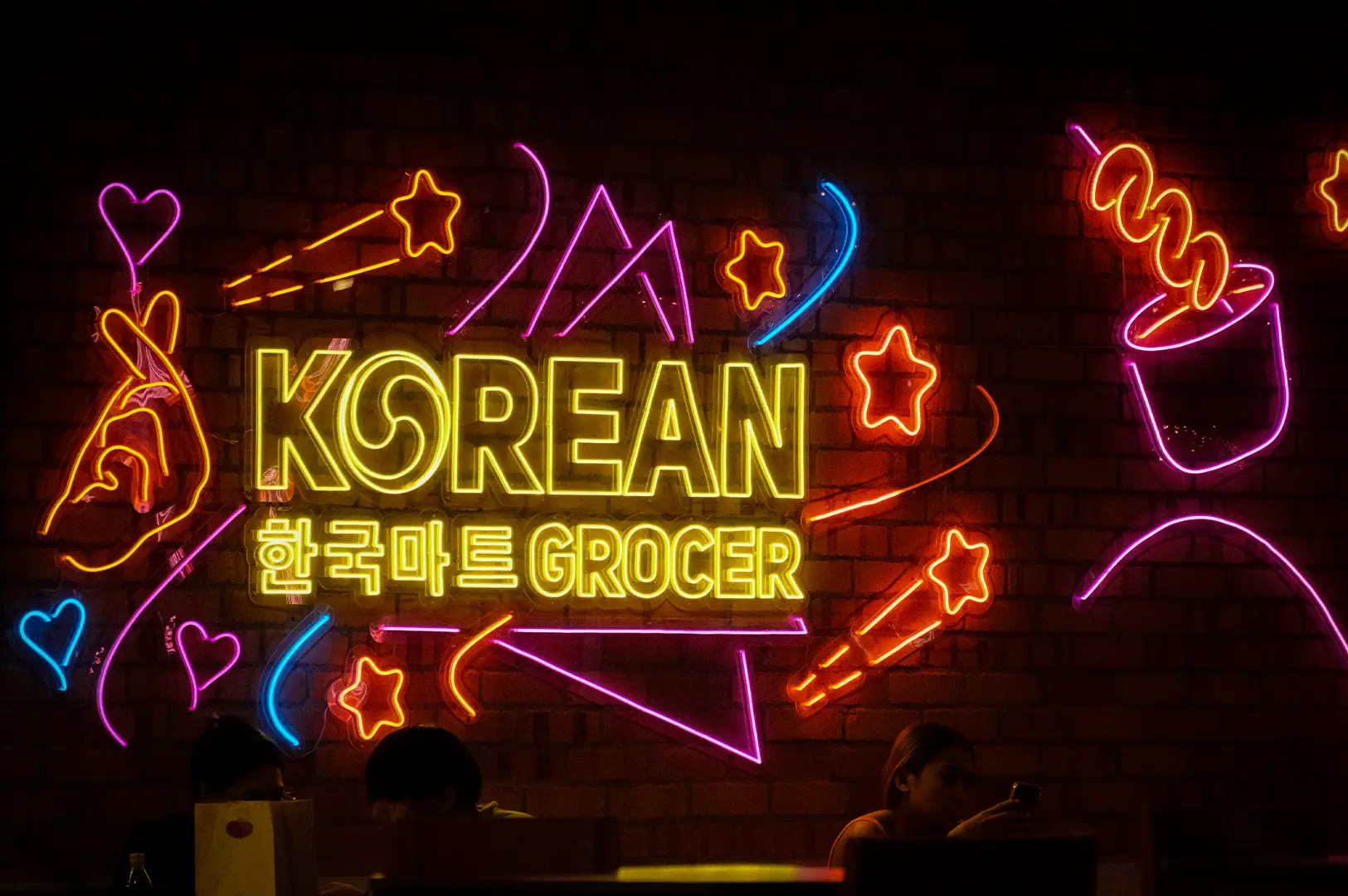 Colorful neon Korean mart sign on a brick wall inside a Korean grocery store in Singapore, featuring vibrant lights and a trendy café-style atmosphere.