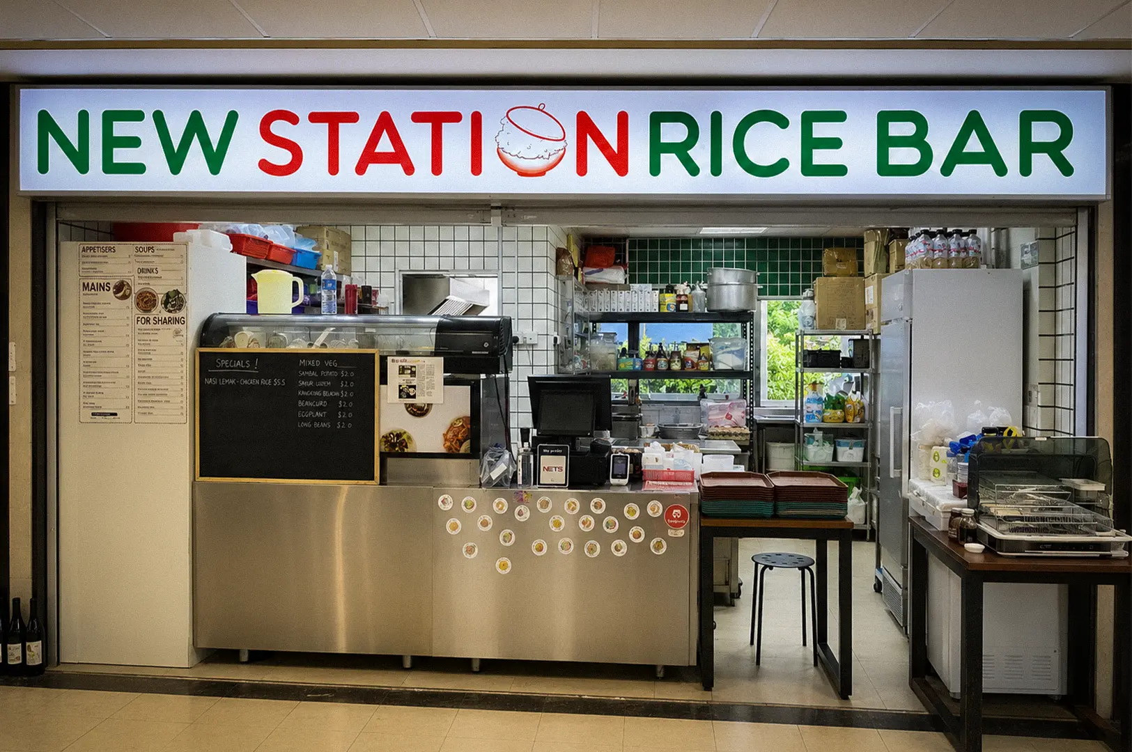 Front entrance of New Station Rice Bar at Fortune Centre in Singapore, featuring the restaurant signage, open kitchen, ordering counter, and casual dining setup.