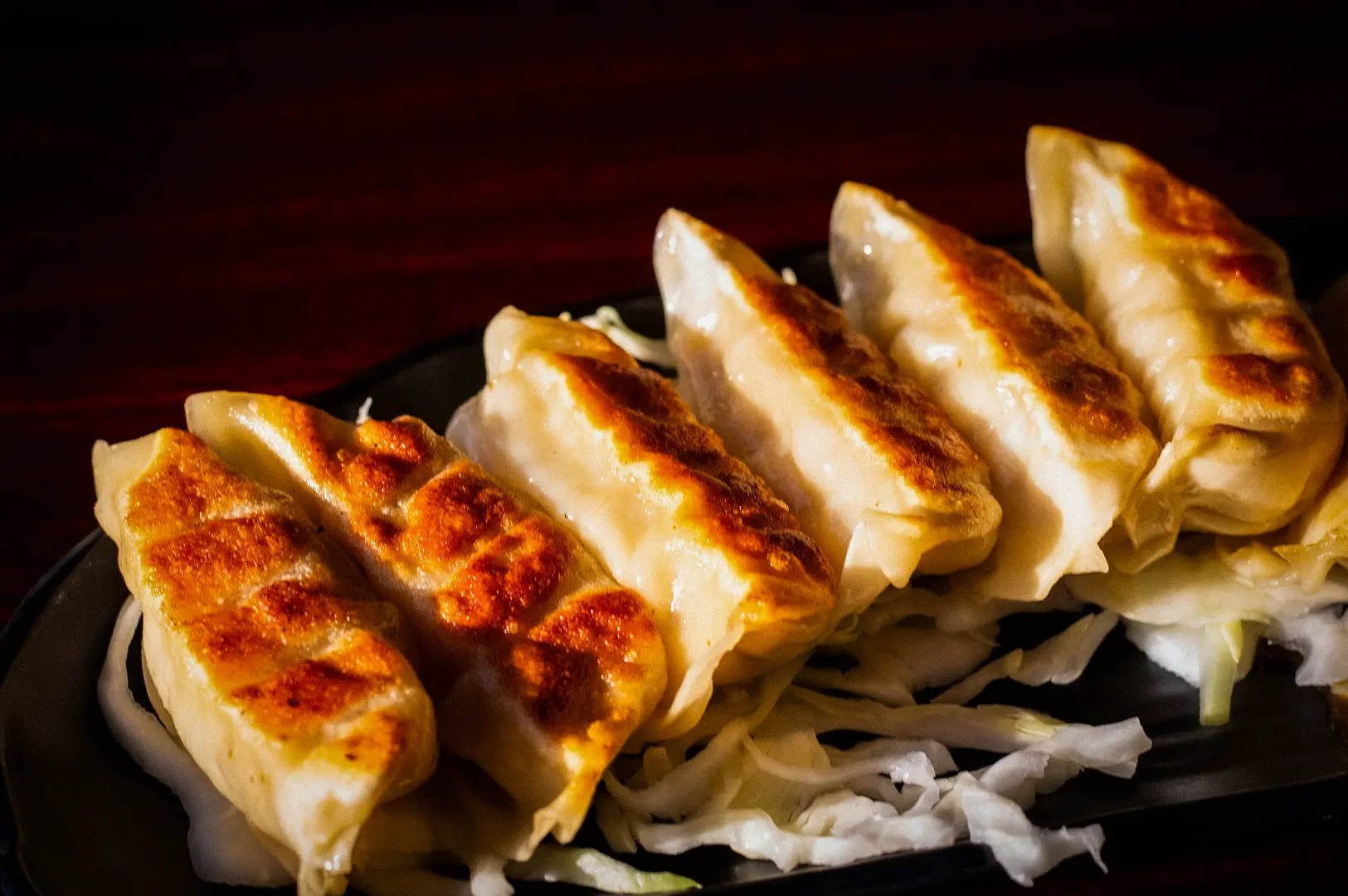 Golden brown pan-fried Japanese gyoza dumplings served on a black plate with shredded cabbage, showcasing crispy bottoms and freshly cooked savory filling.