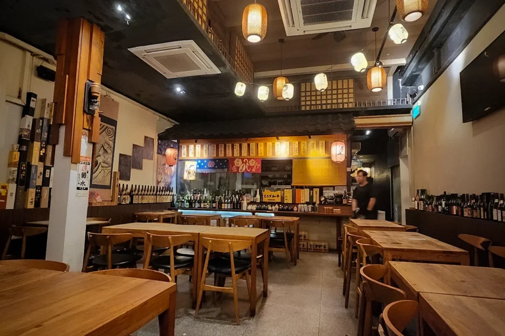 Interior of Shukuu Izakaya Singapore featuring wooden tables, traditional Japanese paper lanterns, a sake bar, and a warm, cozy dining atmosphere.