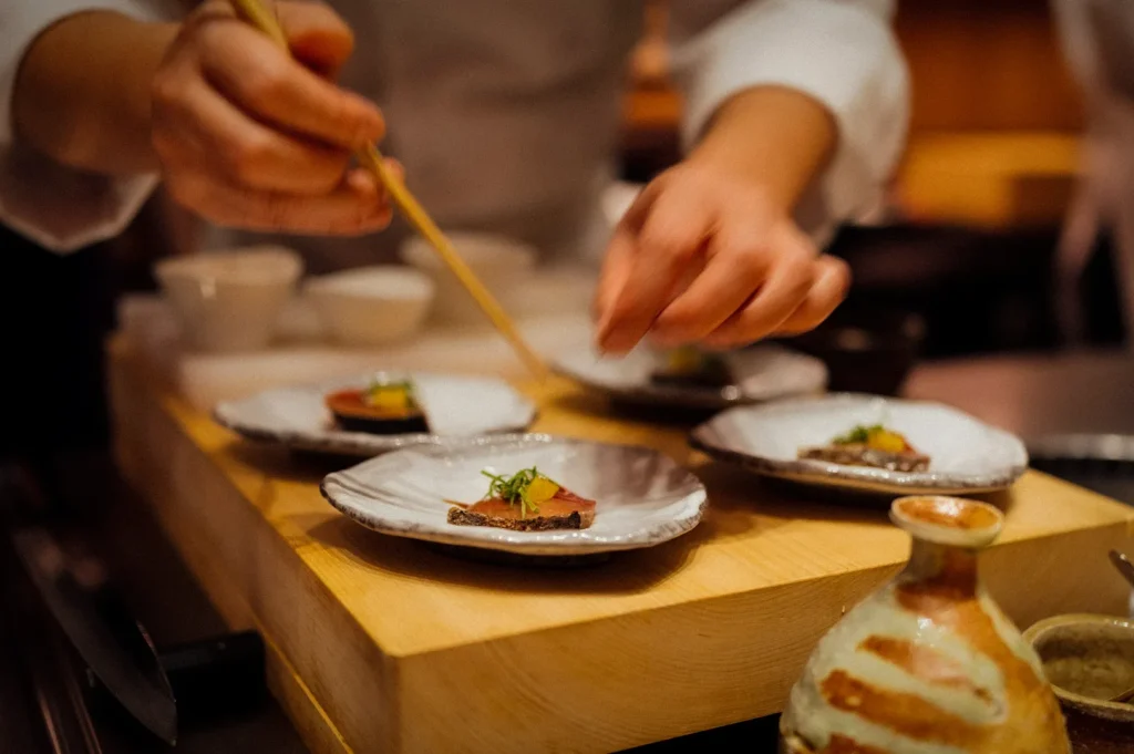 Japanese omakase chef carefully plating premium sushi course dishes on ceramic plates at an intimate fine dining counter.