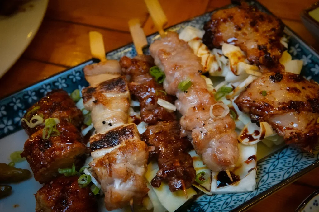 Assorted Japanese yakitori skewers with grilled chicken, pork, and glazed meat served over shredded cabbage on a decorative plate.