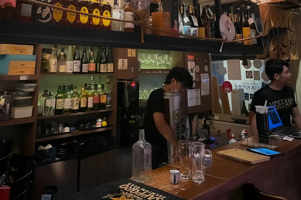 Bar area at Shukuu Japanese Izakaya Singapore featuring illuminated Japanese paper lanterns, sake barrels, whisky and sake bottles, and a warm traditional izakaya atmosphere.