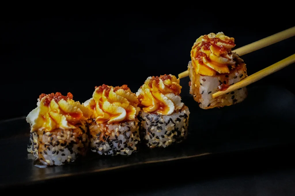 Assorted Japanese nigiri sushi platter with salmon, tuna, shrimp, eel, tamago, crab stick, avocado, soy sauce, and chopsticks on a black background.