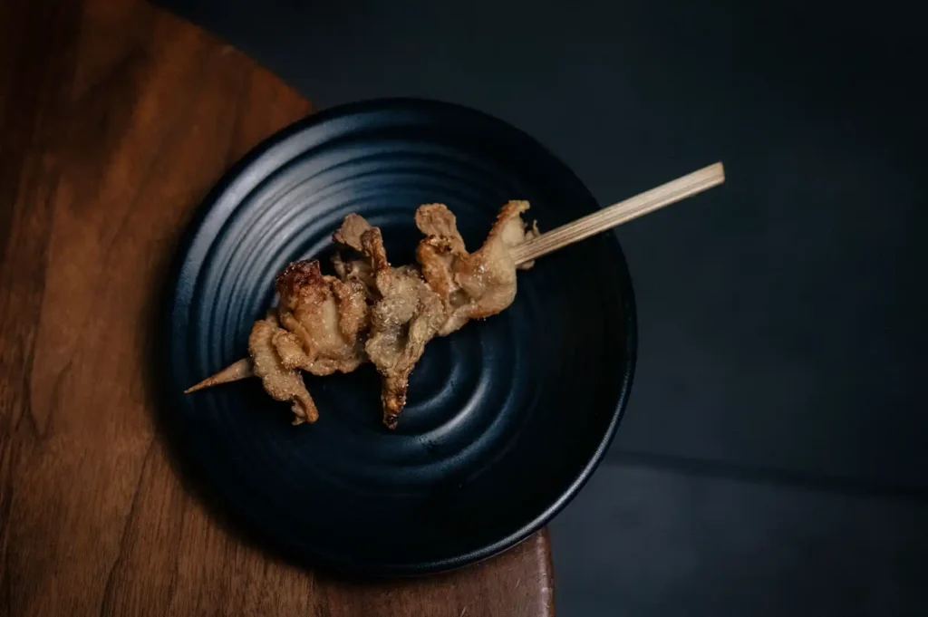 Grilled yakitori chicken skewer served on a black ceramic plate, featuring juicy charcoal-grilled Japanese chicken prepared in traditional izakaya style.
