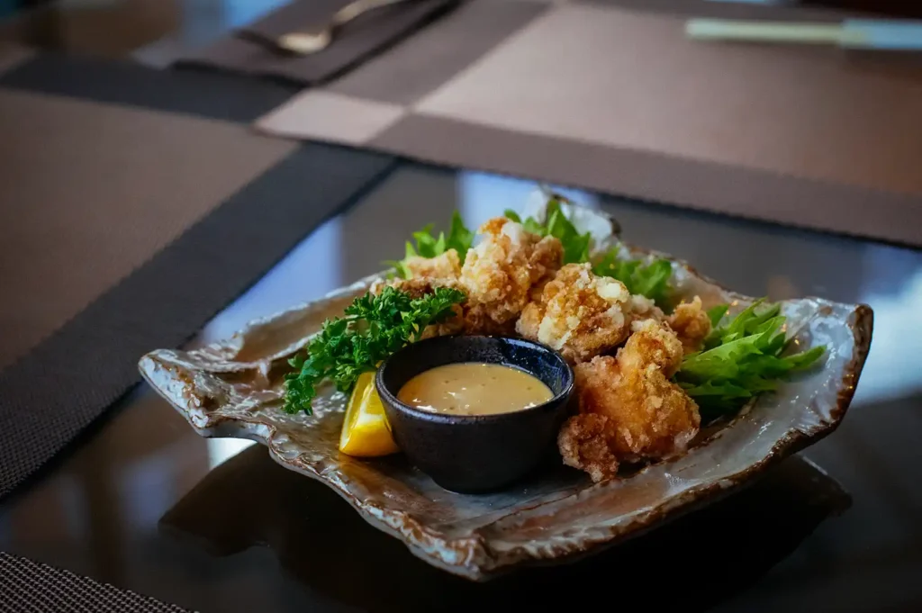 Crispy Japanese chicken karaage served with creamy dipping sauce, fresh greens, parsley, and lemon on a rustic ceramic plate, perfect as an izakaya appetizer.