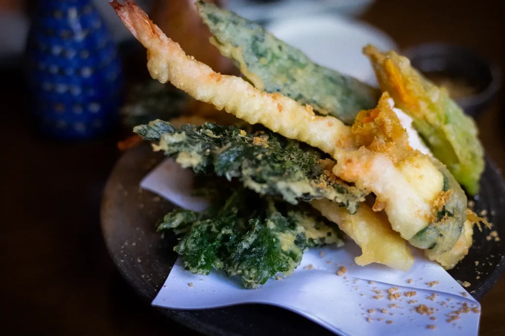 Crispy Japanese tempura featuring shrimp and assorted vegetables, lightly battered and served on a traditional plate with dipping sauce.